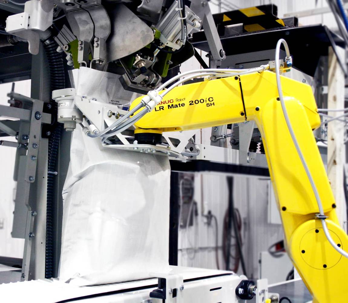 A robotic arm holds an open-mouth bag in place during the filling process