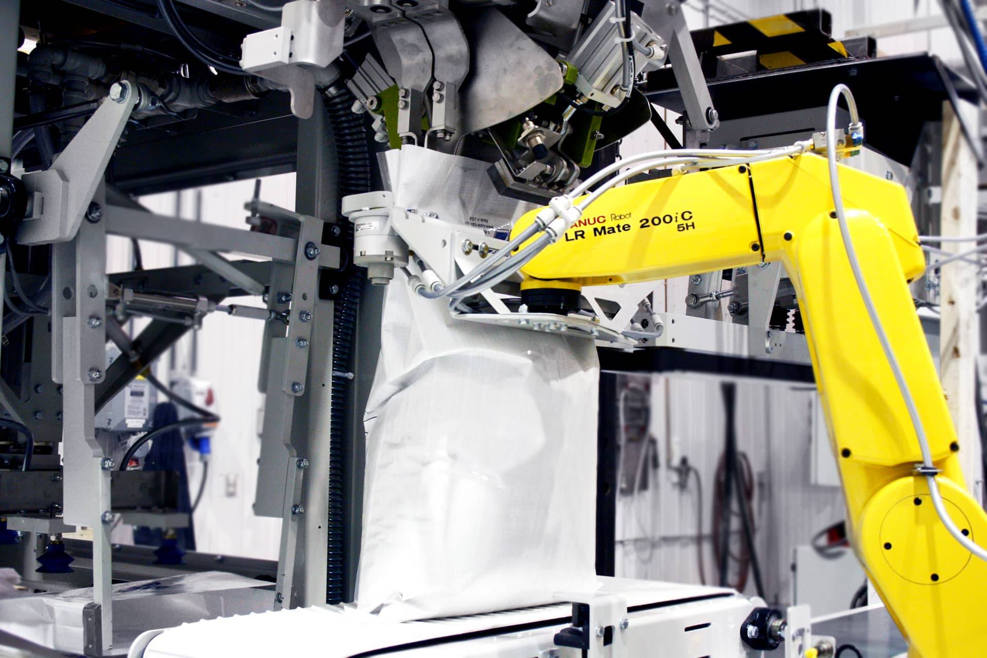 A robotic arm holds an open-mouth bag in place during the filling process